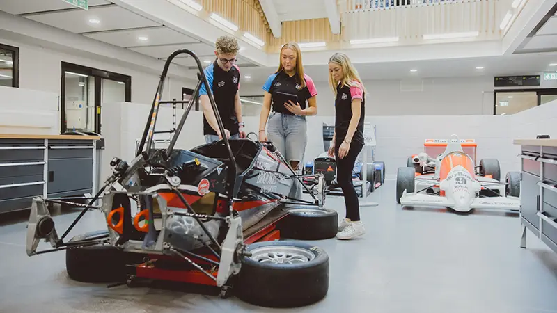 Three students working on a racing car on the ground floor of the Teaching building on the Headington Hill site