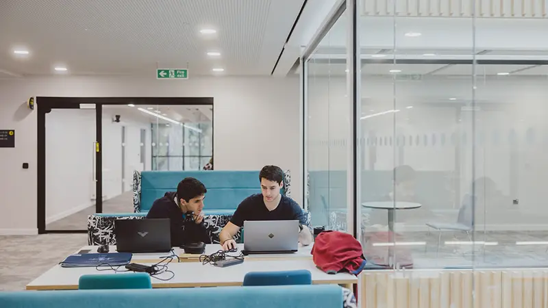 Two students working on laptops in the Teaching building on the Headington Hill site