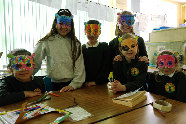 Six smiling pupils standing and sitting at a desk 