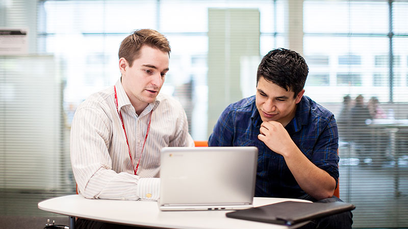 Student and older adult sat at a table looking at a laptop screen