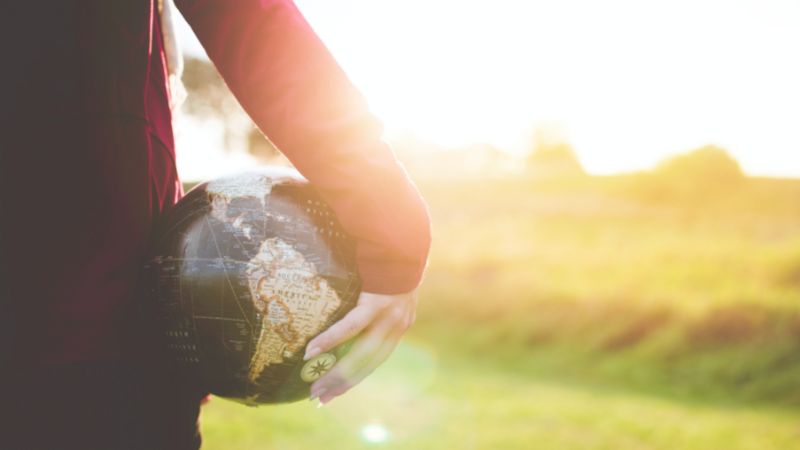 a person standing whilst holding a globe in the sunset