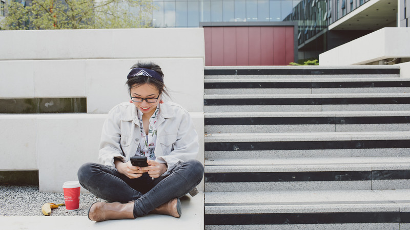 A woman sat near some steps on her phone