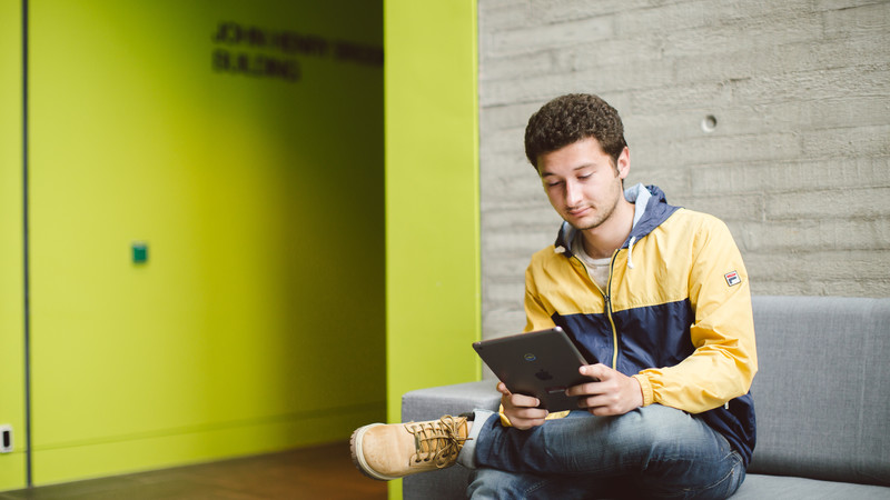 A student sat on a sofa reading a book